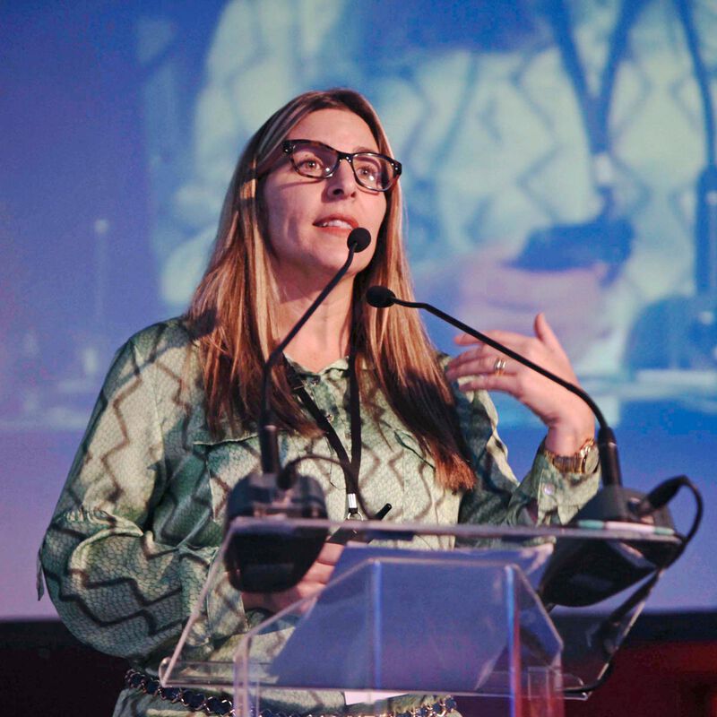 A woman stands at the lectern and gestures with her hands.